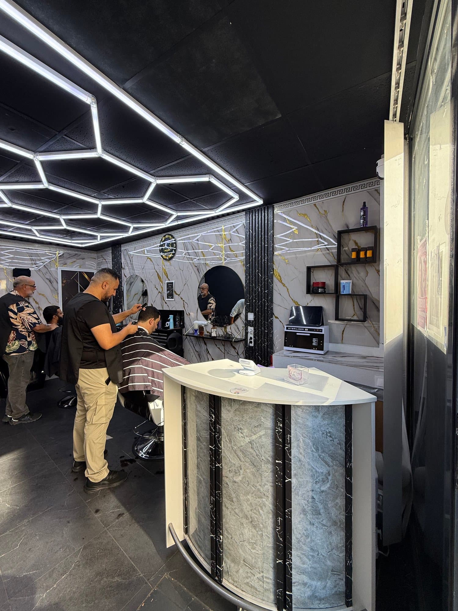 Le comptoir d'accueil en marbre du Côté Barbier, un coiffeur au travail en arrière plan