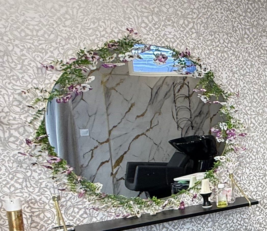 Miroir rond couronné de fleurs mauves au dessus d'un poste de coiffure